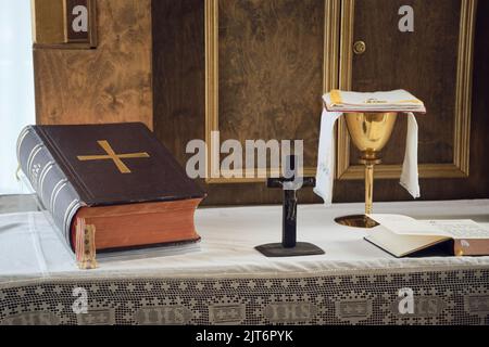 Katholische Symbole Zusammensetzung. Die Bibel, Holzkreuz und goldener Kelch auf dem Altar. Stockfoto