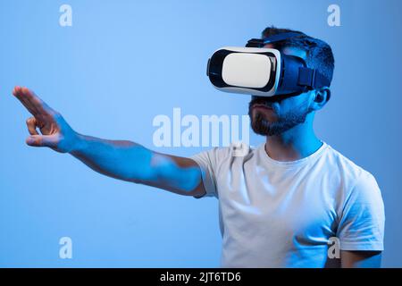 Bärtiger Mann mit VR-Brille und im Metaverse-Gespräch mit Freunden in einem Raum mit blauem Licht. VR-Helm für Unterhaltung, Lernen und Gaming. Stockfoto