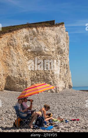 England, East Sussex, Eastbourne, The Seven Sisters Cliffs, The Birling Gap, Familie mit buntem Sonnenschirm Entspannen am Strand Stockfoto