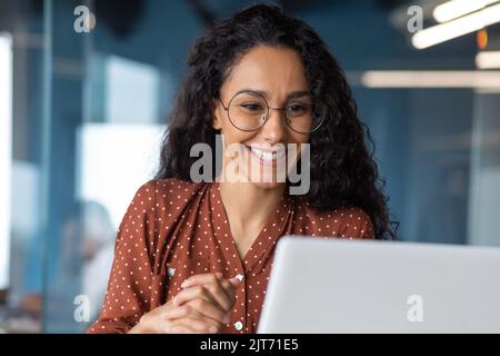 Nahaufnahme einer jungen, schönen Geschäftsfrau mit lockigen Haaren und Brille Hispanic-Frau, die mit einem Laptop für die Fernkommunikation und Konferenz während eines Videoanrufs spricht Stockfoto