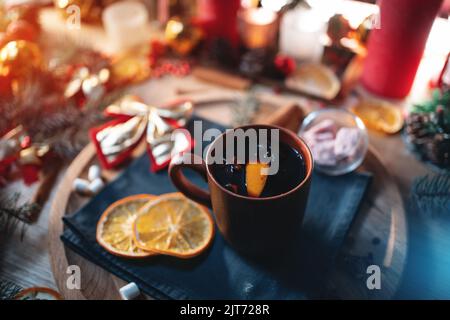 Glühwein aus Rotwein in Tasse mit Orange, weihnachtlicher Dekorationstisch mit Kerzen Stockfoto