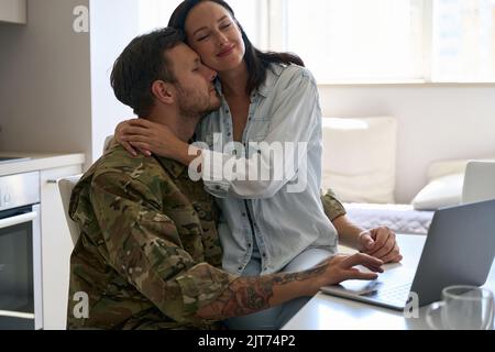 Eine junge Frau umarmte einen Soldaten sanft in Militäruniform Stockfoto