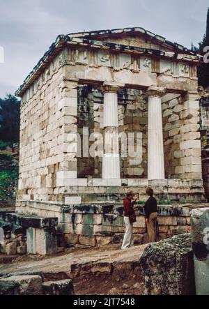 März 1980. Archivscan von einem Dia. Touristen vor der Schatzkammer der Athenen, erbaut, um ihres Sieges bei der Schlacht von Marathon zu gedenken. Delphi, antike Stadt und Sitz des wichtigsten griechischen Tempels und orakels von Apollo im Gebiet von Phocis auf dem steilen unteren Hang des Berges Parnassus, etwa 6 Meilen (10 km) vom Golf von Korinth entfernt. Delphi ist heute eine bedeutende archäologische Stätte mit gut erhaltenen Ruinen. Stockfoto