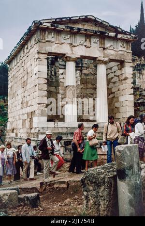 März 1980. Archivscan von einem Dia. Touristen vor der Schatzkammer der Athenen, erbaut, um ihres Sieges bei der Schlacht von Marathon zu gedenken. Delphi, antike Stadt und Sitz des wichtigsten griechischen Tempels und orakels von Apollo im Gebiet von Phocis auf dem steilen unteren Hang des Berges Parnassus, etwa 6 Meilen (10 km) vom Golf von Korinth entfernt. Delphi ist heute eine bedeutende archäologische Stätte mit gut erhaltenen Ruinen. Stockfoto