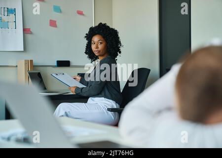 Frau, die einen Kollegen ansieht, der am Tisch eingeschlafen ist Stockfoto