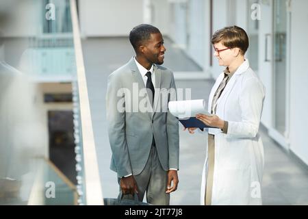 Hochwinkelporträt eines lächelnden afroamerikanischen Geschäftsmannes, der mit einer Kollegin in der Halle des Bürogebäudes spricht Stockfoto