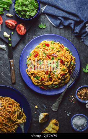 Spaghetti mit Tomatensauce, rotem Pfeffer und grüner Zwiebel serviert mit geröstetem Brot und Gewürzen auf dunklem Hintergrund. Stockfoto