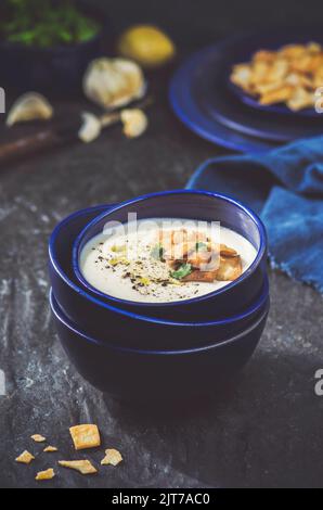 Köstliche warme Suppe mit gerösteten Croutons, Tropfen nativem Olivenöl und frischer Petersilie auf dunklem Grund. Stockfoto