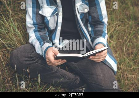 Ein Mann in einem karierten Hemd liest in der Natur ein Buch. Stockfoto