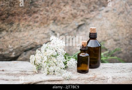 Kleine braune Medizinflasche auf natürlichem Hintergrund mit weißen Schafgarben-Blüten. Stockfoto