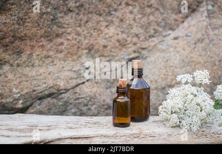 Kleine braune Medizinflasche auf natürlichem Hintergrund mit weißen Schafgarben-Blüten. Stockfoto