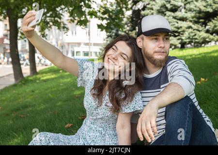 Ein Mann und ein Mädchen machen ein Selfie, das auf dem Gras im Park sitzt. Stockfoto