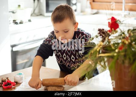 Ein Junge bereitet in der Küche Lebkuchen zu. Weihnachtstraditionen der Familie. Freizeit des Kindes während der Neujahrsferien. Stockfoto