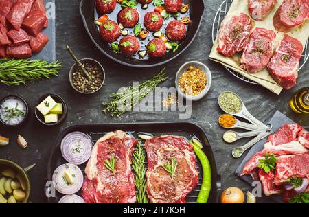 Verschiedene Arten von frischem rohem Fleisch mit Gewürzen bestreut und mit Bio-Zutaten auf dunklem Hintergrund platziert. Draufsicht mit Nahaufnahme. Stockfoto