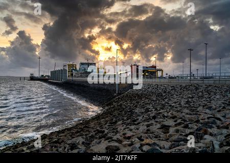 Eine Aufnahme eines bewölkten Sonnenuntergangs an einem Sandstrand mit einem Hafen und einem Haus in der Nähe Stockfoto