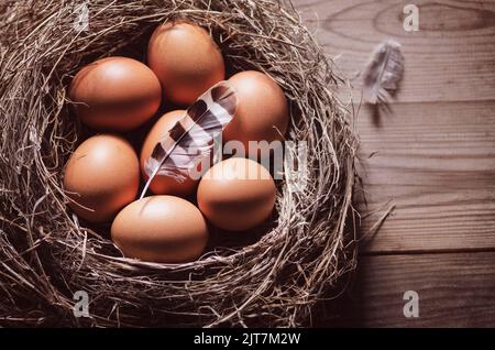 Stillleben mit Nahaufnahme von rohen Hühnereiern im Nest auf rustikalem Holzhintergrund. Stockfoto