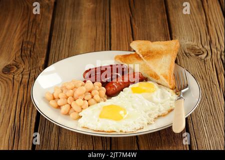 Komplettes englisches Frühstück mit Eiern, Würstchen, Bohnen und Toast auf Holzgrund Stockfoto