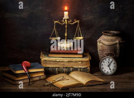 Klassisches Stillleben mit Vintage-Büchern, die mit einer beleuchteten Kerze auf Justice Scale, Uhr, Pfeife, antikem Glas und Gläsern auf rustikalem Hintergrund platziert sind. Stockfoto