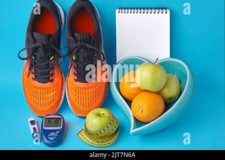 Orangefarbene Turnschuhe, Tagebuch-Notizbuch, Glucometer, Maßband und Früchte auf blauem Hintergrund Stockfoto