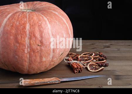 Schöner großer orangefarbener Kürbis und getrocknete Gewürze für die Konfitüre auf einem Holztisch auf dunklem Grund Stockfoto