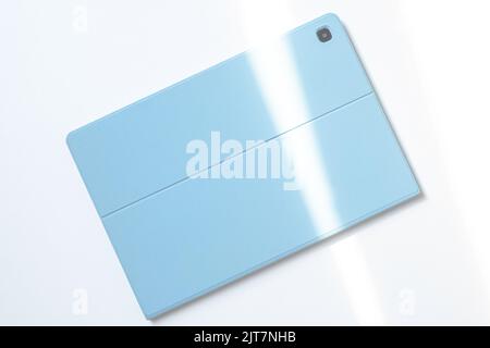 Ein Tablet in einer blauen Hülle auf einem weißen Schreibtisch. Die Lichter einer Sonne. Stockfoto