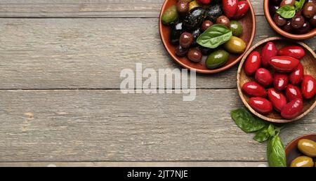 Teller mit verschiedenen Arten von leckeren Oliven auf Holzhintergrund mit Platz für Text Stockfoto