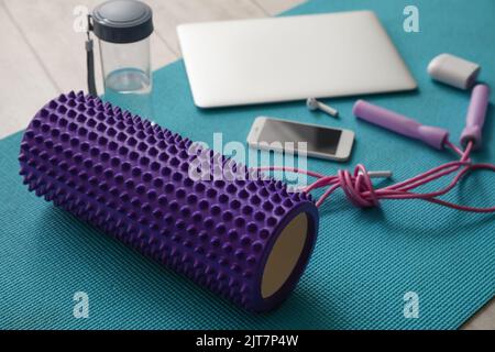 Schaumstoffrolle mit Springseil, Wasserflasche und Geräten auf Matte im Zimmer Stockfoto