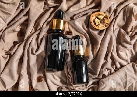 Zusammensetzung mit Flaschen ätherischen Öls und Kaffeebohnen auf Stoffhintergrund Stockfoto