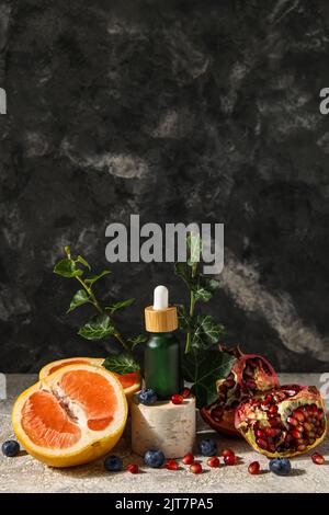 Zusammensetzung mit einer Flasche ätherisches Öl, Früchten und Beeren auf dem Tisch Stockfoto
