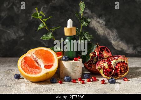 Zusammensetzung mit einer Flasche ätherisches Öl, Früchten und Beeren auf dem Tisch Stockfoto