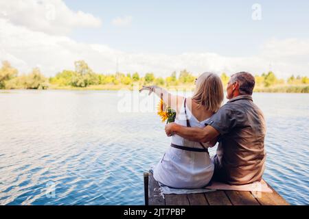 Ein Paar mit einer älteren Familie, das sich am Sommerfluss entspannt. Mann und Frau genießen die Landschaft, die auf dem Pier in die Ferne zeigt Stockfoto