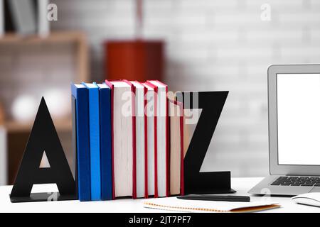 Stilvoller Halter mit Büchern und Laptop auf dem Tisch im Zimmer Stockfoto