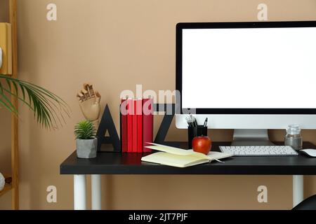 Moderner Arbeitsplatz mit Computer, Buchhalter, Apfel- und Stifttasse in der Nähe einer beigefarbenen Wand im Zimmer Stockfoto