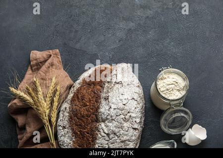 Roggenbrot mit Stacheletts, Serviette und Mehlkrug auf dunklem Grund Stockfoto