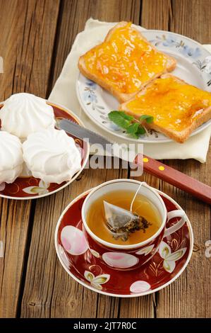 Grüner Tee, zefir und Toast mit orangefarbener Marmelade auf Holzhintergrund vertikal Stockfoto