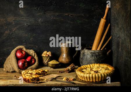 Klassisches Stillleben mit Apfelkuchen mit rotem Apfel und frischen Zutaten auf rustikalem Holzhintergrund. Stockfoto