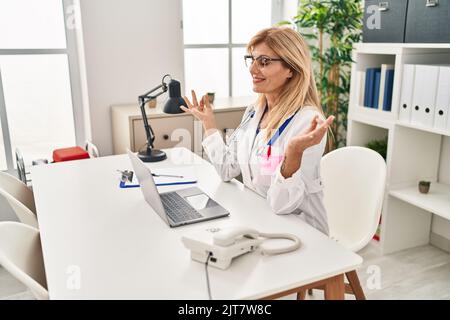 Blonde Frau mittleren Alters in der Ärzteinform, die in der Klinik Yoga-Übungen macht Stockfoto