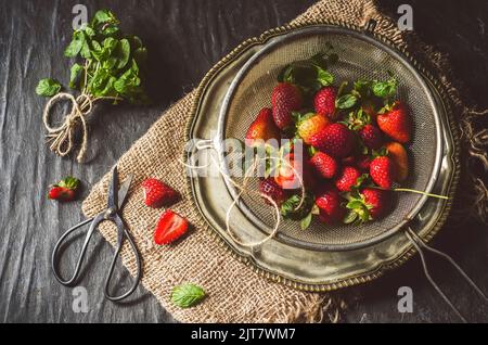 Frische Erdbeeren mit frischer Minze auf rustikalem dunklen Hintergrund. Draufsicht mit Nahaufnahme. Stockfoto