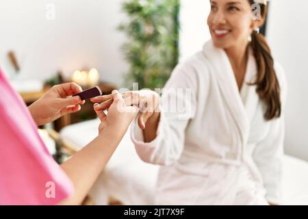 Junge latinerin im Bademantel bei Maniküre-Sitzung Stockfoto