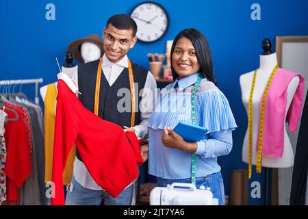 Mann und Frau Schneiderinnen halten Touchpad und T-Shirt im Nähstudio Stockfoto