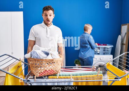 Hispanische Mutter und Sohn hängen Kleidung an der Wäscheleine erschrocken und erstaunt mit offenem Mund für Überraschung, Unglauben Gesicht Stockfoto