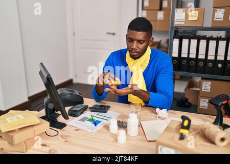 Junge afroamerikanische Mann E-Commerce-Business-Arbeitnehmer Einnahme Pillen Behandlung im Büro Stockfoto