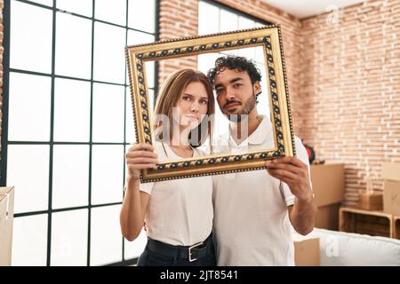 Junge zwei Menschen, die leeren Rahmen mit ernstem Gesichtsausdruck zusammenhalten, entspannen sich. Einfach und natürlich auf die Kamera schauen. Stockfoto