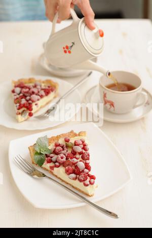 Zwei Stück Beerenkuchen mit Schlagsahne und einer Tasse Tee auf weißem Hintergrund Stockfoto