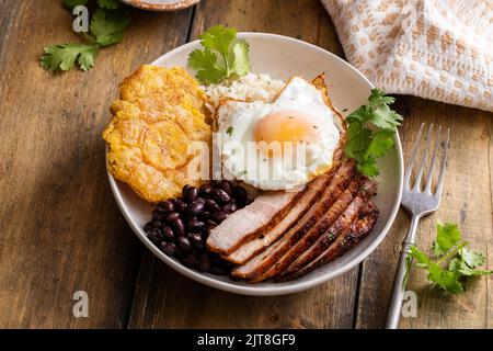 Karibisches oder lateinamerikanisches Frühstück mit Reis, Bohnen, Tostones und Schweinefleisch in Scheiben und Spiegelei Stockfoto