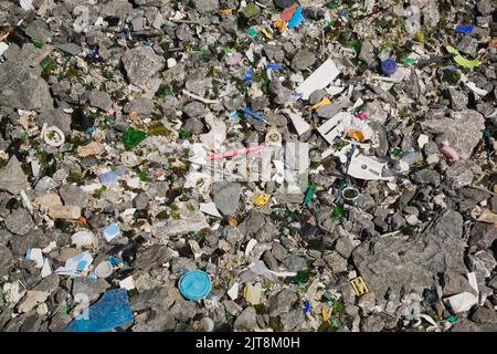 Weggeworfene Kunststoffe, Glas und andere Ablagerungen auf dem Boden am Abfallentsorgungsstandort. Stockfoto