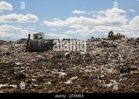 Schwere Maschinen verteilen sich und verdichten weggeworfene Abfälle und Abfälle am Abfallwirtschaftsstandort. Stockfoto