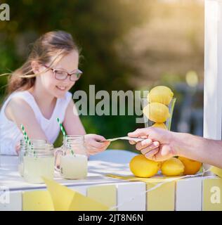 Ihre Getränke verkaufen sich schnell. Ein kleines Mädchen verkauft Limonade von ihrem Stand draußen. Stockfoto