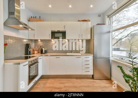 Offene Küche mit Schränken aus dunklem Holz und Pendelleuchten in luxuriösem Apartment Stockfoto