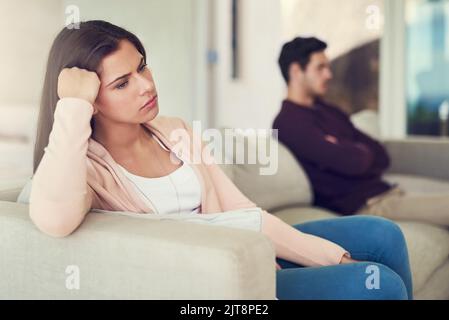 Ich kann gar nicht glauben, dass ich über etwas so kleines gestritten habe. Ein unglückliches Paar, das nach einem Streit zu Hause auf einem Sofa getrennt voneinander saß. Stockfoto